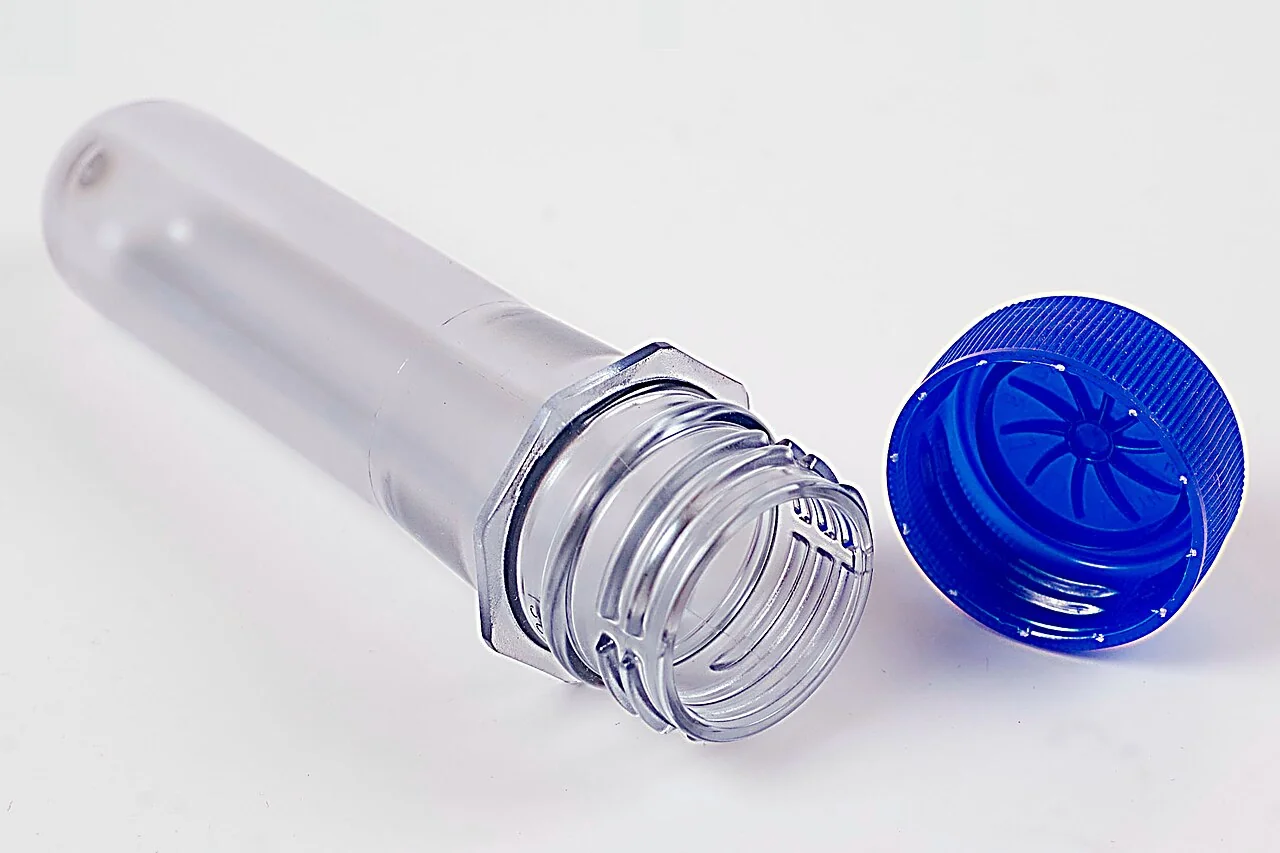 A clear PET bottle preform beside a blue screw cap.